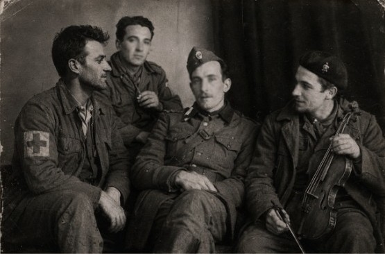 Fotografía antigua de cuatro hombres de uniforme, uno con brazalete de la Cruz Roja y otro con un violín